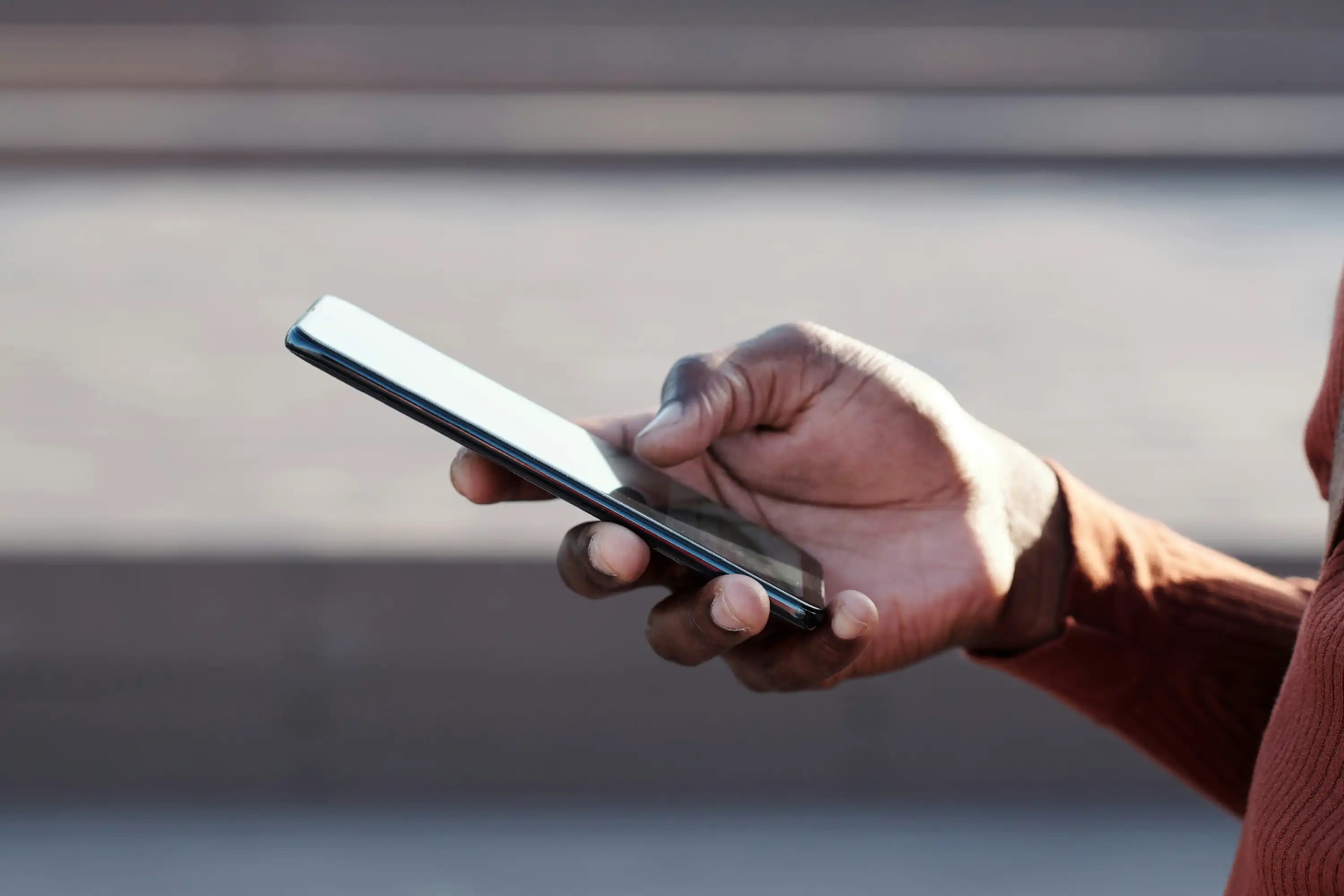 Close-up of a hand holding a smartphone with a white screen, outdoors. 