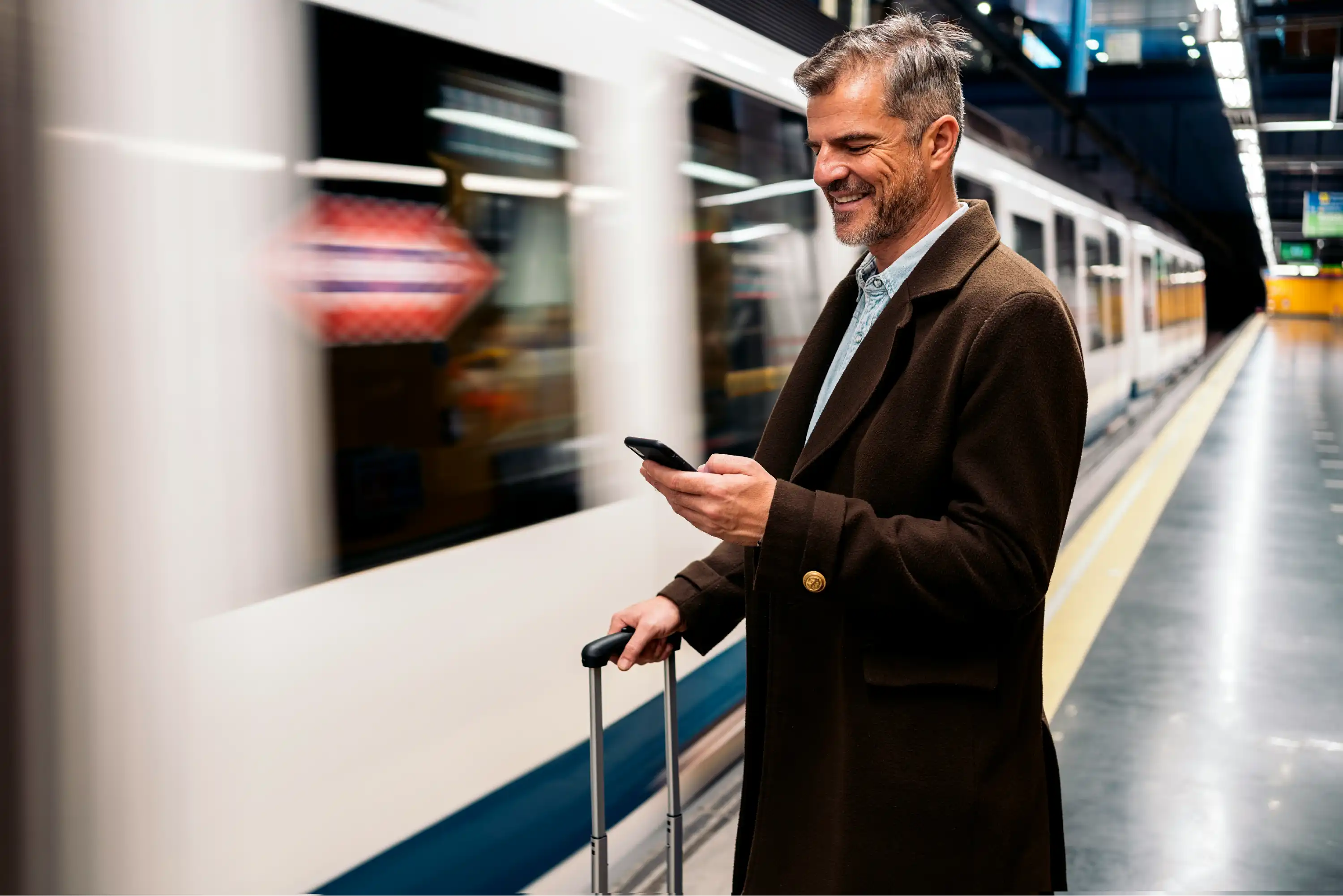 Business traveller using his phone on a train platform with a suitcase